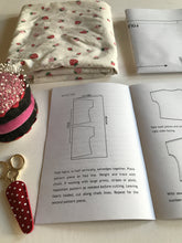 open instruction booklet, with folded fabric and sewing pattern, pin cushion and small scissors in a polkadot holder