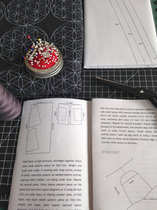 open instruction booklet with scissors, folded sewing pattern and fabric, pin cushion and spool of thread